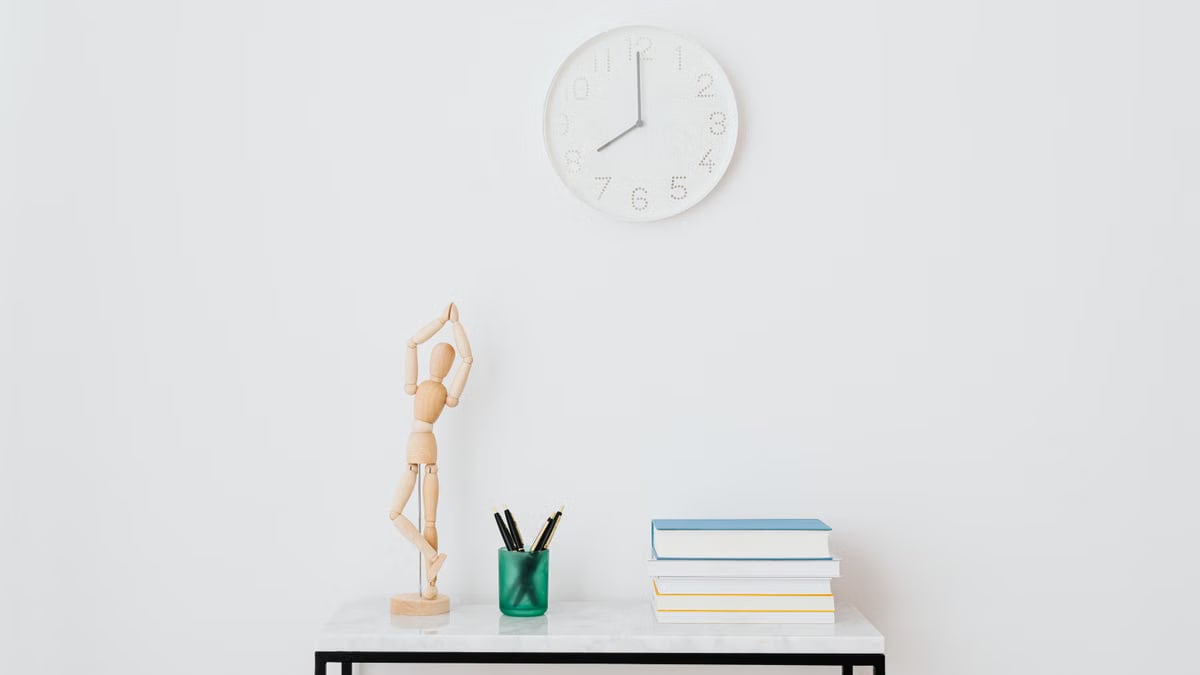 A minimalist workspace setup featuring books, a clock, and decorative elements on a white wall.